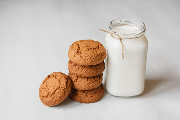 Milk in a glass jar and oatmeal cookies on a white table background. Copy, empty space for text