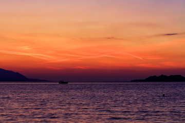 Silhouette of a sea boat running along the horizon of the sea line against the backdrop of a beautiful, vibrant sunset on the Gulf of Corinth.