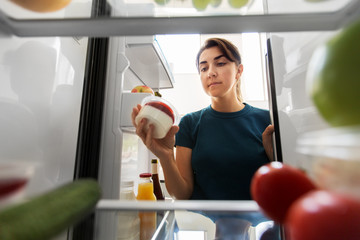 healthy eating, food and diet concept - woman taking yoghurt from fridge at home kitchen