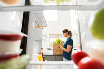 healthy eating, diet and food concept - view to woman with paper bag and lettuce from home fridge