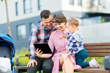 family, leisure and technology concept - happy mother, father and little son with tablet computer sitting on street bench in city