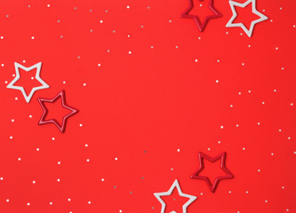 Christmas composition frame made of confetti and star ornaments on red background