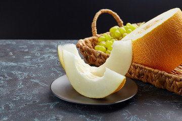 Beautiful still life with a melon on a dark background. Sliced slices on a black plate.