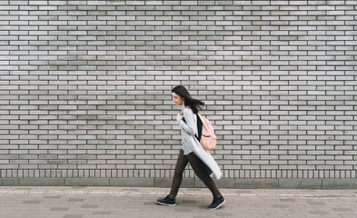 Fototapeta na wymiar Young beautiful caucasian woman in gray pullover with a pink bag walking on the autumn street. Brick wall.