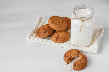 Milk in glass jar and oatmeal cookies near napkin on white table background. Copy, empty space for text