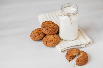 Milk in glass jar and oatmeal cookies near napkin on white table background. Copy, empty space for text