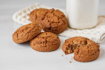 Milk in glass jar and oatmeal cookies near napkin on white table background. Copy, empty space for text