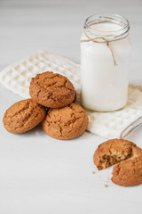 Milk in glass jar and oatmeal cookies near napkin on white table background. Copy, empty space for text