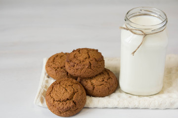 Milk in glass jar and oatmeal cookies near napkin on white table background. Copy, empty space for text
