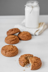 Milk in glass jar and oatmeal cookies near napkin on white table background. Copy, empty space for text