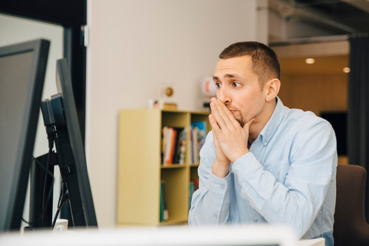 Thoughtful programmer with hands clasped looking at computer monitor while working at desk in office
