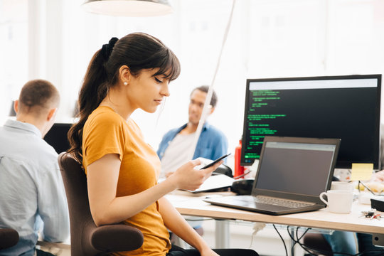 Female computer programmer using smart phone while sitting at desk in office