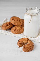 Milk in glass jar and oatmeal cookies near napkin on white table background. Copy, empty space for text