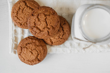 Milk in glass jar and oatmeal cookies near napkin on white table background. Top view. Copy, empty space for text