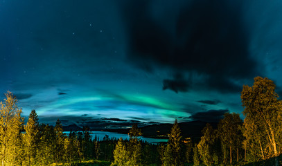 Aurora Borealis and heavy clouds over Norwegian mountains around Rossvatnet Lake, Northern Norway. Late summer night.