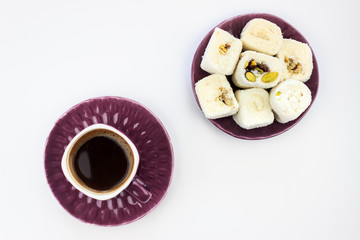 Top view of Turkish coffee with foam on purple cup and white Turkish delight with pistachio on isolated white background