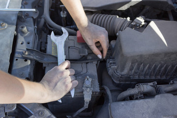 Car battery repair under the hood, female hands car repair