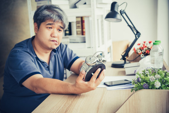 Blurred of Asian midle-ages man, He is patient from neurological diseases, or hemiplegia having a facial palsy, He is looking at the alarm clock in his hand, to health and paralysis concept.