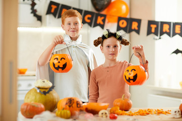 Portrait of cute boy and girl holding lanterns and smiling at camera while visiting Halloween party