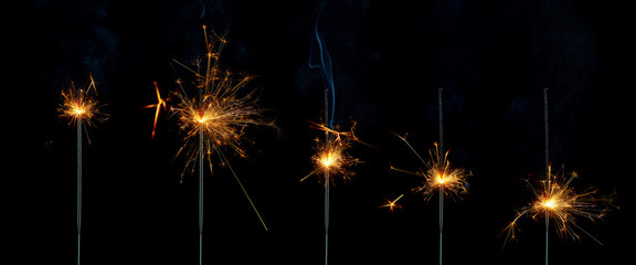 Five lighted sparklers at different stages of burning on a black background. Isolated image.