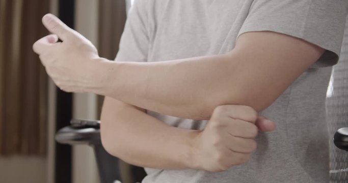 Asian man massaging on his elbow pain while sitting on a chair in living room at home.healthcare and medical concepts.