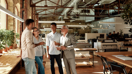 Discussing new project. Four colleagues holding coffee cups and talking about something while...