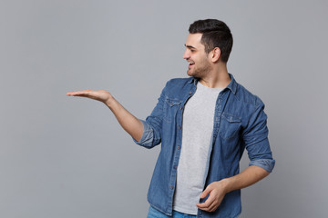 Handsome stylish unshaven young man in denim jeans shirt posing isolated on grey wall background...