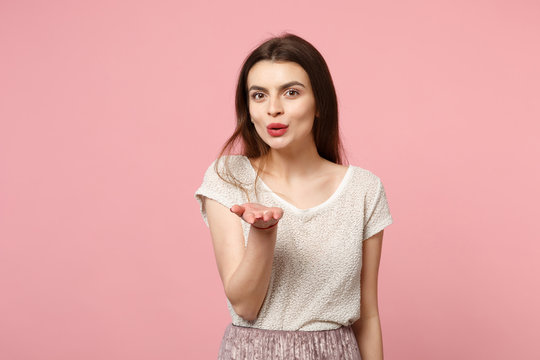 Pretty young woman in casual light clothes posing isolated on pastel pink wall background, studio portrait. People sincere emotions lifestyle concept. Mock up copy space. Blowing sending air kiss.