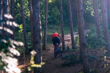 Obraz premium Fit cyclist riding his bike downhill through a forest ( woods ) while wearing a red shirt and red shoes.