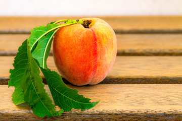 Peach with foliage lies on wooden boards.