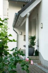 A house with pitched roof and 2 gables has a covered entrance. In the foreground roses are blooming. © Tanja Esser