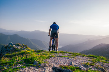 Adventurous Cyclist riding his mountain bike at the edge of a cliff, on rocky terrain while wearing...