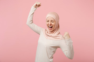Happy young arabian muslim woman in hijab light clothes posing isolated on pink background. People...