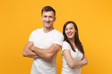 Smiling young couple two friends guy girls in white blank empty design t-shirts posing isolated on yellow orange wall background. People lifestyle concept. Mock up copy space. Holding hands crossed.