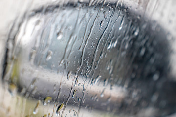 Rain drops rolling on window in storm, and a blurred black car side view mirror on a background, close up