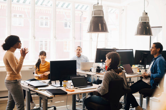 Female computer programmer discussing with coworkers at desk during meeting