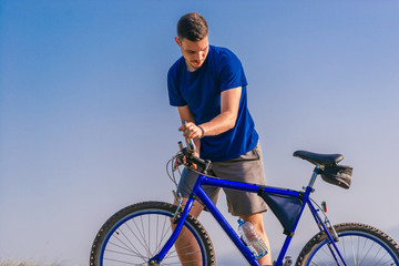 Fit male mountain biker pushing his bike uphill while looking exhausted on a sunny summer day.