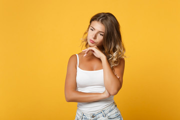 Pensive young girl in light casual clothes posing isolated on yellow orange background in studio. People sincere emotions lifestyle concept. Mock up copy space. Looking aside put hand prop up on chin.