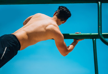 Beautiful male athlete exercising on parallel bars, doing push-ups