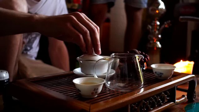 Chinese tea ceremony. Close up of hand take the teapot and pouring the hot tea into the glass serving jar with ceramic tea cup set on the table.