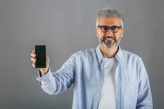 middle aged man holding smartphone with blank screen isolated