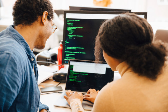 Female computer hacker explaining male coworker over laptop on desk in office