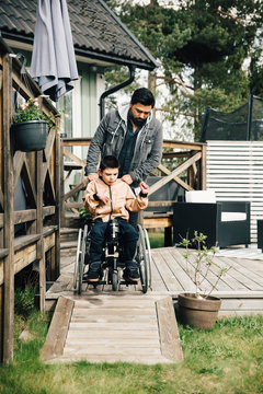 Father pushing autistic son sitting on wheelchair in backyard