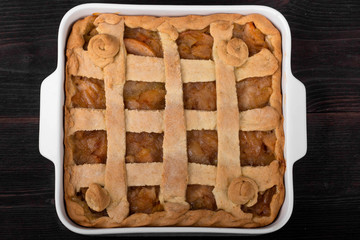 Apple pie in a square ceramic baking sheet on a dark wooden background