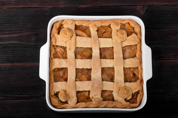 Apple pie in a square ceramic baking sheet on a dark wooden background
