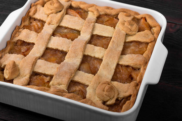Apple pie in a square ceramic baking sheet on a dark wooden background