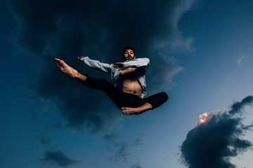 Fototapeta na wymiar Positive young man is dancing over blue sky