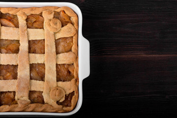 Apple pie in a square ceramic baking sheet on a dark wooden background