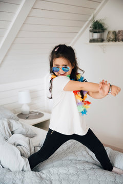 Portrait of happy girl wearing sunglasses dancing on bed at home