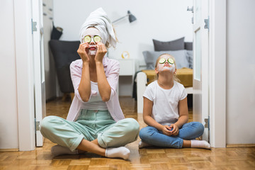 mother and daughter meditating at home with cosmetic face mask applied